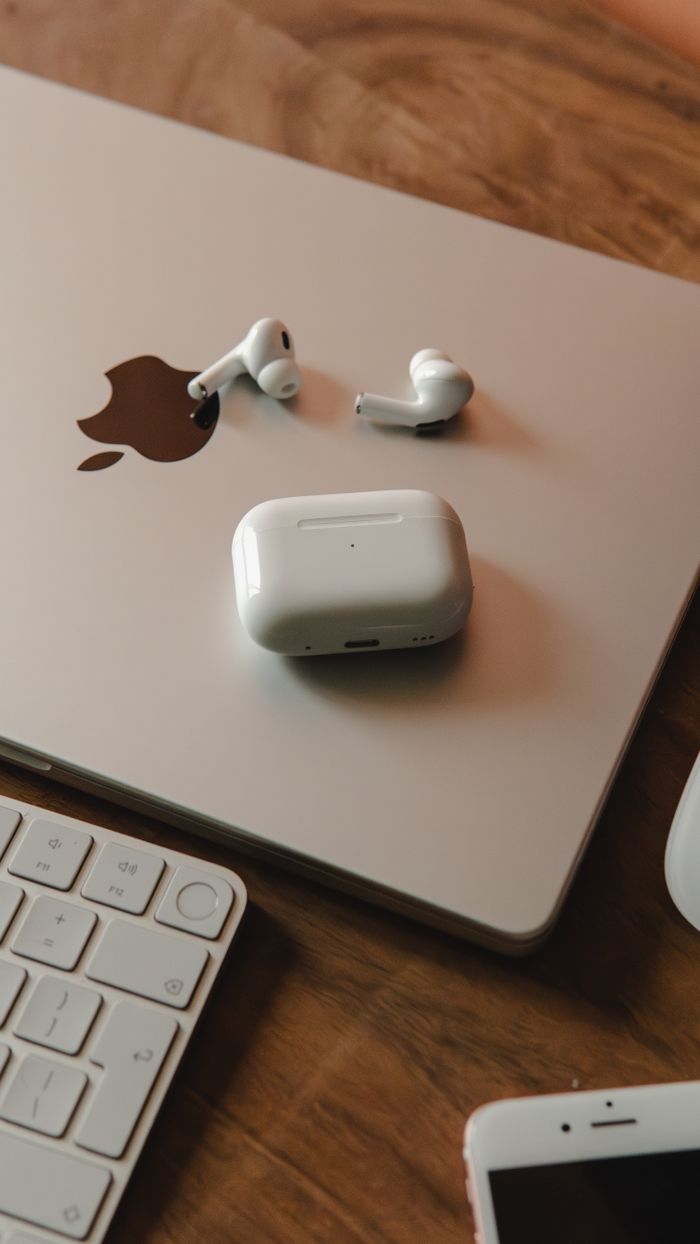 MacBook with wireless earphones and keyboard on a wooden desk, a tech-savvy workspace.